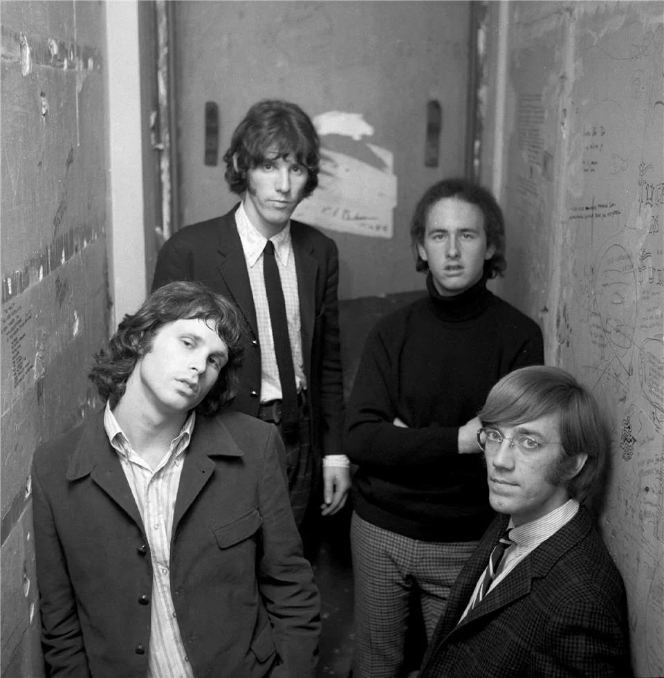 The Doors grubunun dört üyesinin bir koridorda samimi bir pozda durduğu siyah-beyaz fotoğraf.
