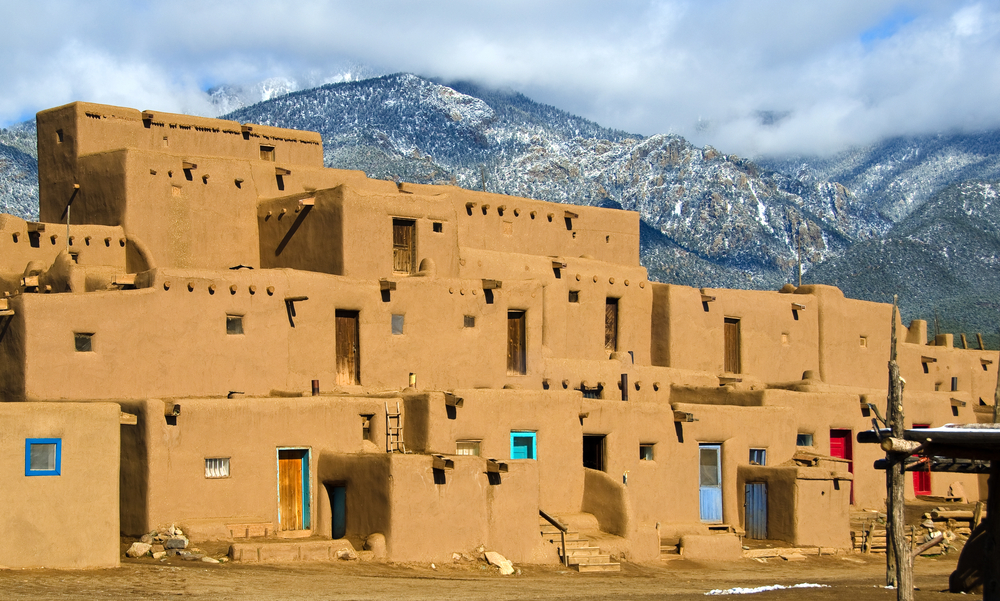 Taos, New Mexico'daki geleneksel Pueblo tarzı binalar, karlı dağ manzarası ile birlikte.